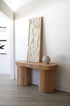 a wooden bench sitting next to a white vase on top of a hard wood floor