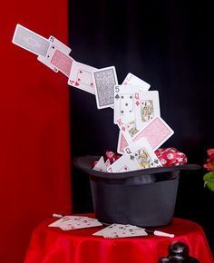 playing cards fall into a black bucket on a red tablecloth with flowers in the background