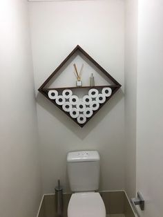 a white toilet sitting in a bathroom next to a wooden shelf filled with toilet paper