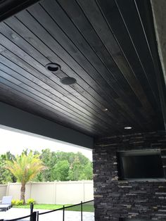 an outdoor living area with stone fireplace and flat screen tv mounted on the wall above it