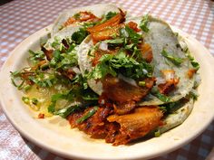 a white plate topped with tacos covered in lettuce and meat on top of a checkered table cloth