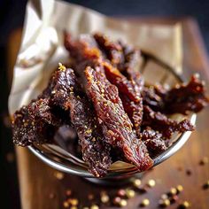 a glass bowl filled with bacon strips on top of a wooden table