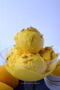 a bowl filled with yellow ice cream next to some lemons and oranges on a table