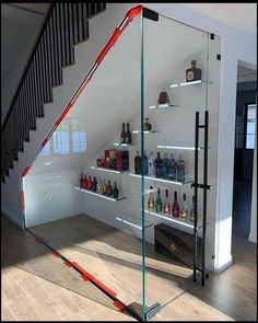 a glass shelf with bottles on it next to a stair case in a room that has white walls and wooden floors