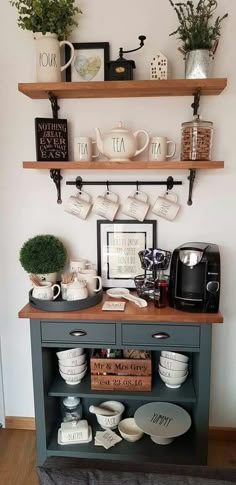 a coffee bar with cups and plates on the shelf above it is decorated with greenery