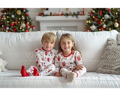 two young children sitting on a couch in pajamas with christmas trees in the back ground