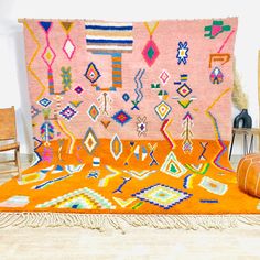 an orange rug with colorful designs and fringes on the floor next to a chair