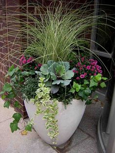 a white planter filled with lots of flowers and greenery next to a door