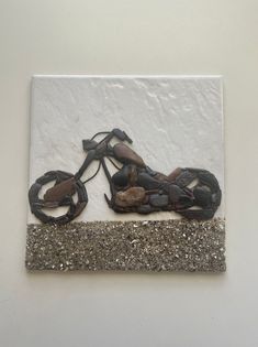 a metal motorcycle is mounted on a white wall with gravel and rocks in the foreground