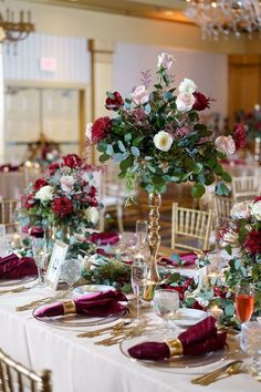 the table is set with white and red linens, gold place settings, and tall centerpieces