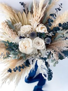 an arrangement of flowers and foliage on a white background with blue ribbon in the center