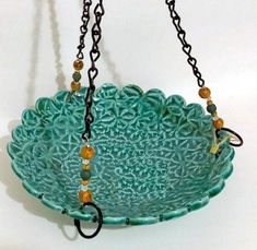 a green bowl with chains hanging from it's sides and beads on the bottom