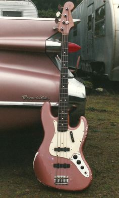 an electric bass guitar sitting on the ground in front of a classic car and trailer