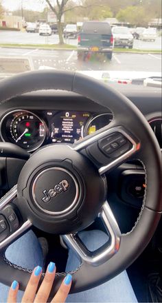 a woman driving a car with her hands on the steering wheel and blue nail polish