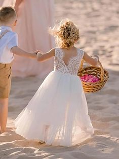 a little boy and girl holding hands while walking on the beach with other people in the background