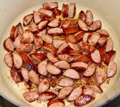 sausages and onions cooking in a pan on the stove top with brown liquid over them