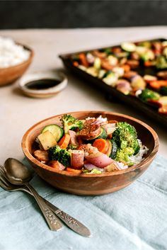 a wooden bowl filled with vegetables next to a tray of rice and other food on a table