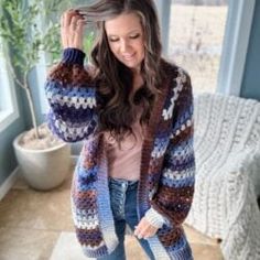 a woman standing in front of a window wearing a colorful cardigan sweater and jeans