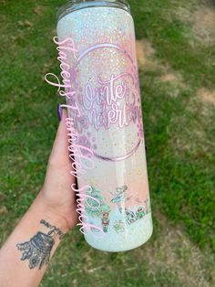 a person holding up a pink and blue glittered tumbler with the words little mermaid on it