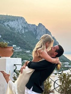 a man holding a woman in his arms on top of a balcony next to the ocean