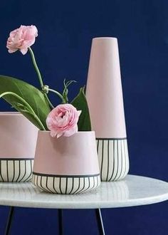 three pink vases with flowers in them on a white and black cake stand against a blue background