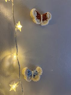 two crocheted butterflies are hanging on the wall next to some string lights and stars