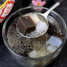 a spoon full of ice cubes sitting on top of a glass bowl filled with liquid