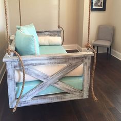 a swing bed made out of wood and rope with pillows on the bottom, sitting in a living room