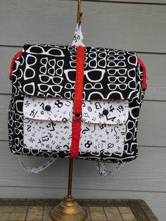 a black and white handbag with red straps on a wooden table next to a gray wall