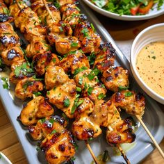 chicken skewers with sauce and vegetables on a platter