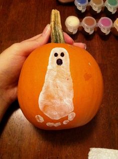 someone is holding a pumpkin with a ghost drawn on it and some other crafting supplies nearby