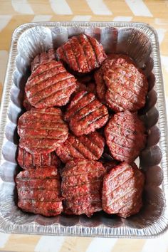 some meat patties in a metal pan on a wooden table with white and gray stripes