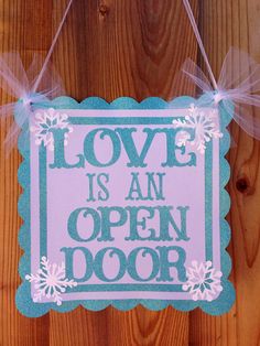 a sign that says love is an open door hanging on a wooden wall with ribbon around it