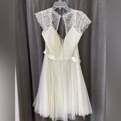 a white dress hanging on a hanger in front of a gray curtain with sheer fabric