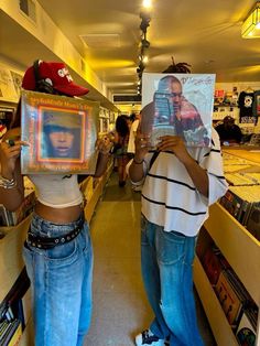 two people standing in a store holding up pictures and books to their faces with the same image on them