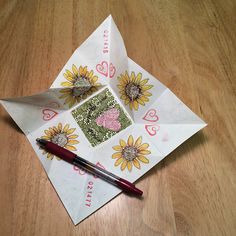 an origami heart with sunflowers on it and a pen resting on top