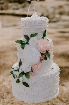 a three tiered cake with white frosting and pink flowers on the top is hanging from a rope