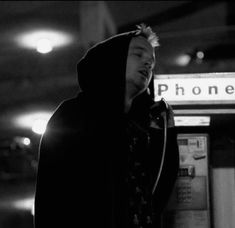 a man in a hoodie standing next to a pay phone booth with his eyes closed