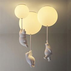 three white lamps hanging from the ceiling with bears and balls attached to each lamp fixture