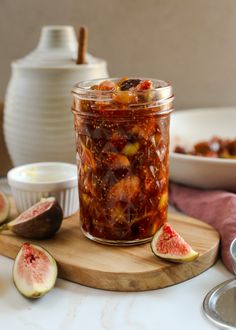 a jar filled with pickled figs sitting on top of a cutting board next to other dishes