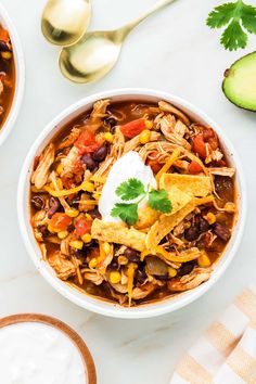 two bowls of chicken tortilla soup with sour cream and avocado on the side