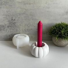 a red candle is sitting in a white holder next to a small potted plant