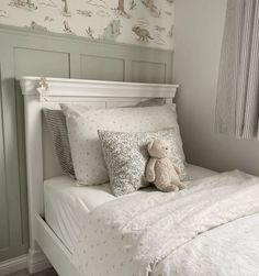 a teddy bear sitting on top of a white bed in a room with wallpaper