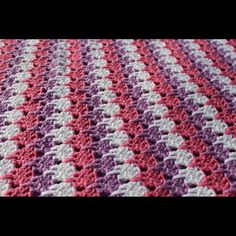 a crocheted blanket with pink, white and purple squares on top of it