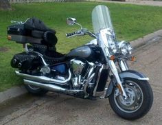 the motorcycle is parked on the side of the road in front of some grass and trees