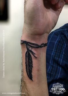 a man's wrist tattoo with a black feather and barbed wire on the wrist