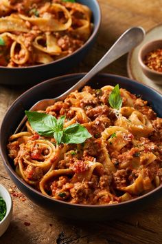 two bowls filled with pasta and sauce on top of a wooden table