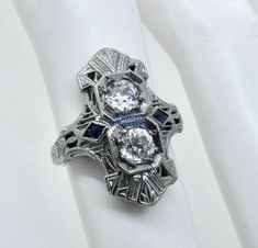 Thank you for viewing this beautiful antique Art Deco 1920's 18k white gold diamond and French cut sapphire ring.  The ring contains 2 old European cut diamonds weighting approximately .70 carats.  The diamonds are an average quality of G/H color and VS clarity.  The French cut sapphires are synthetic which were almost universally used in these type of rings from the time period.  The ring size is 4.75.  The weight of the ring is 3.2 grams.  The ring comes with an attractive gift box.  An import Antique Sapphire Jewelry With Single Cut Diamonds, Art Deco Three Stone Platinum Jewelry, Antique Platinum Three-stone Jewelry, Vintage Diamond White Sapphire Jewelry, Vintage Sapphire Jewelry In Diamond White, Art Deco Sapphire Diamond Ring In Diamond White, Victorian White Gold Jewelry With Vvs Clarity, Art Deco Sapphire Ring In Platinum, Art Deco Sapphire Diamond White Ring