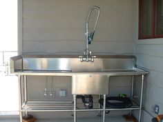 a stainless steel sink sitting on top of a metal shelf next to a wall mounted faucet