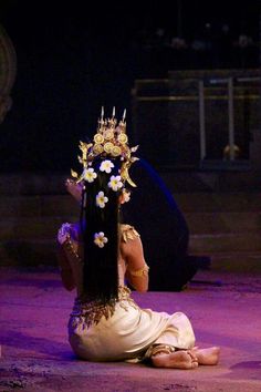 a woman sitting on the ground with a crown on her head and flowers in her hair